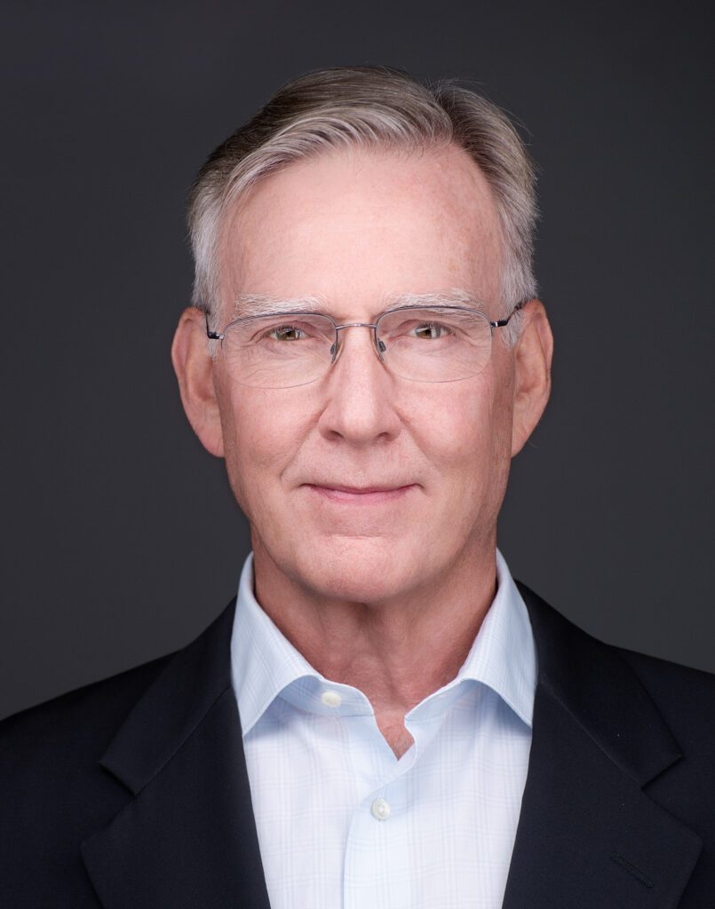 Professional headshot of an older man wearing glasses and a suit jacket.
