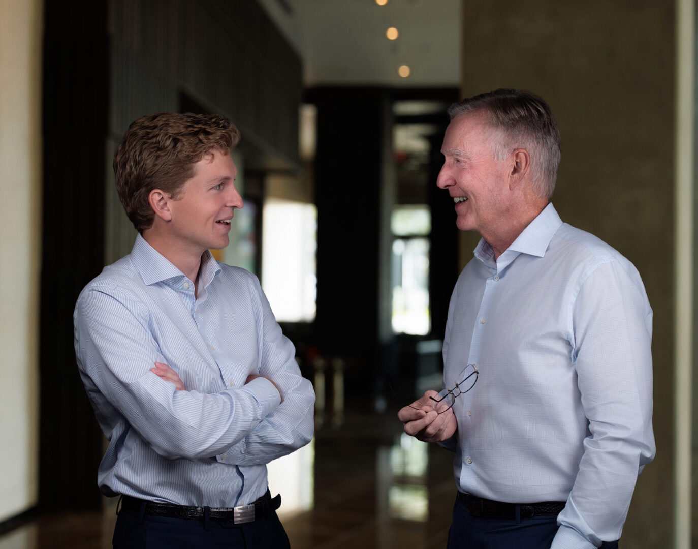 Two men engaged in a friendly conversation indoors, both smiling.
